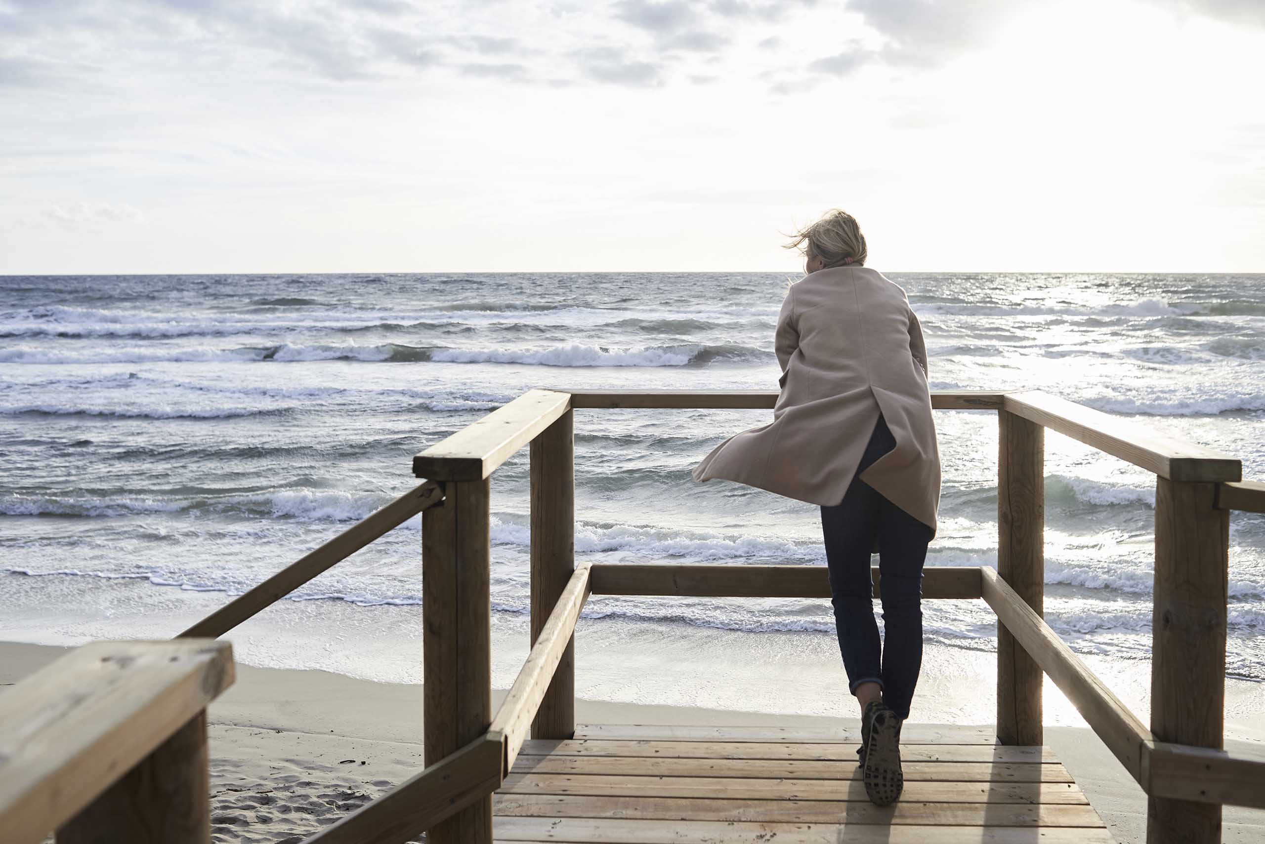 Nainen seisoo aidan vieressä meren rannalla